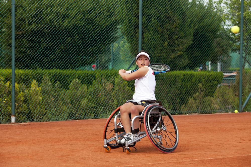 Young female wheelchair tennis player during game.