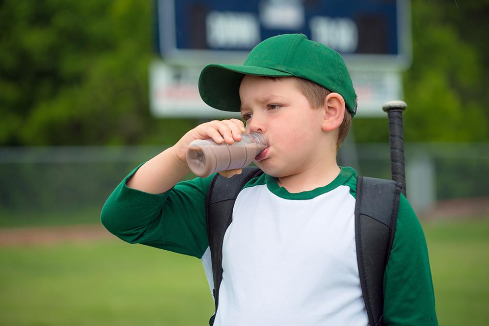 Young white male baseball player drinking chocolate milk.