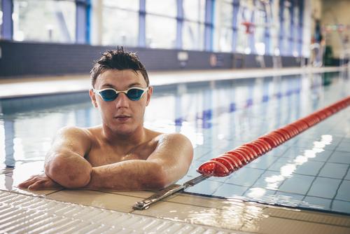 Male amputee swimmer with goggles in pool.