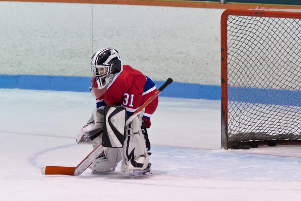 Young kid hockey goalie alone in front of goal on ice.