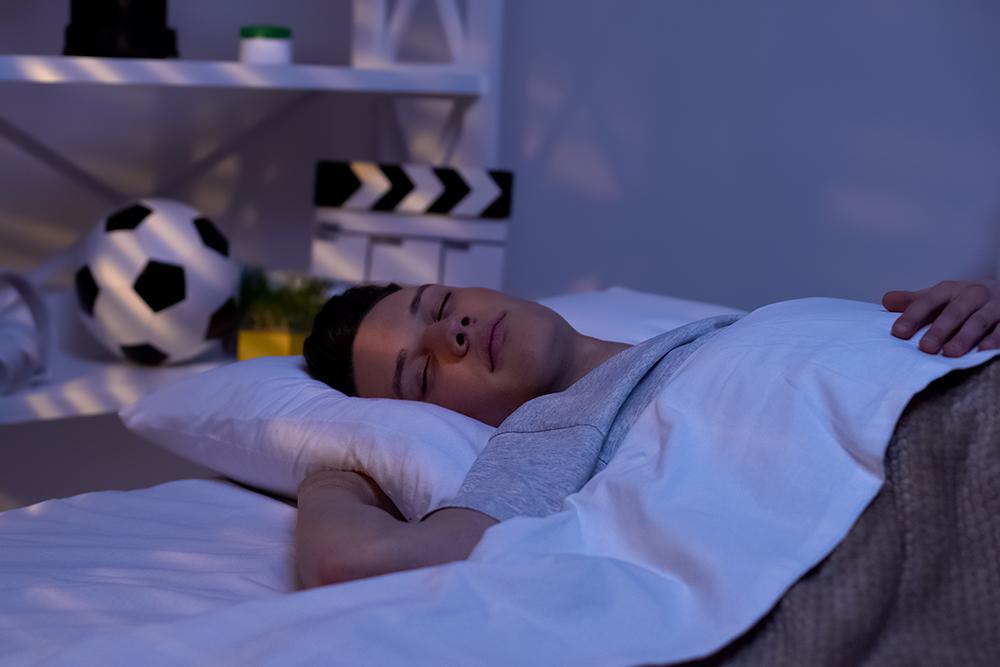 Young black teen asleep with a soccer ball on the shelf behind him.