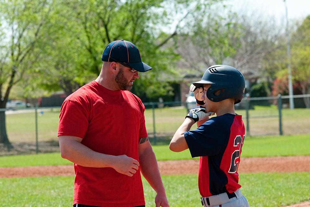 Baseball coach talking to young male athlete.