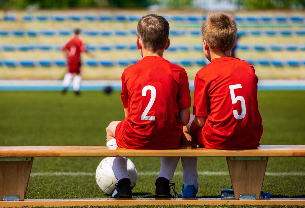 Two young boys on bench during soccer game.