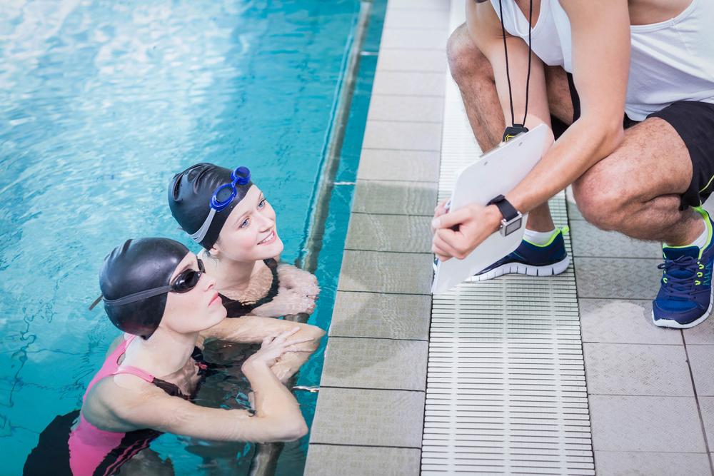 Swimming coach talking to two female swimming athletes.