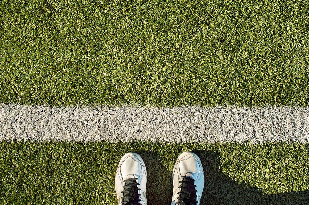 Sneakers toeing a line on a field.