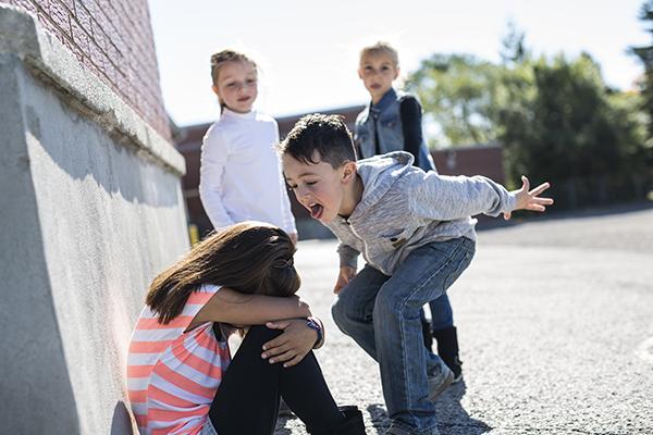 Young white boy yelling at a girl sitting on the ground with her head in her hands.