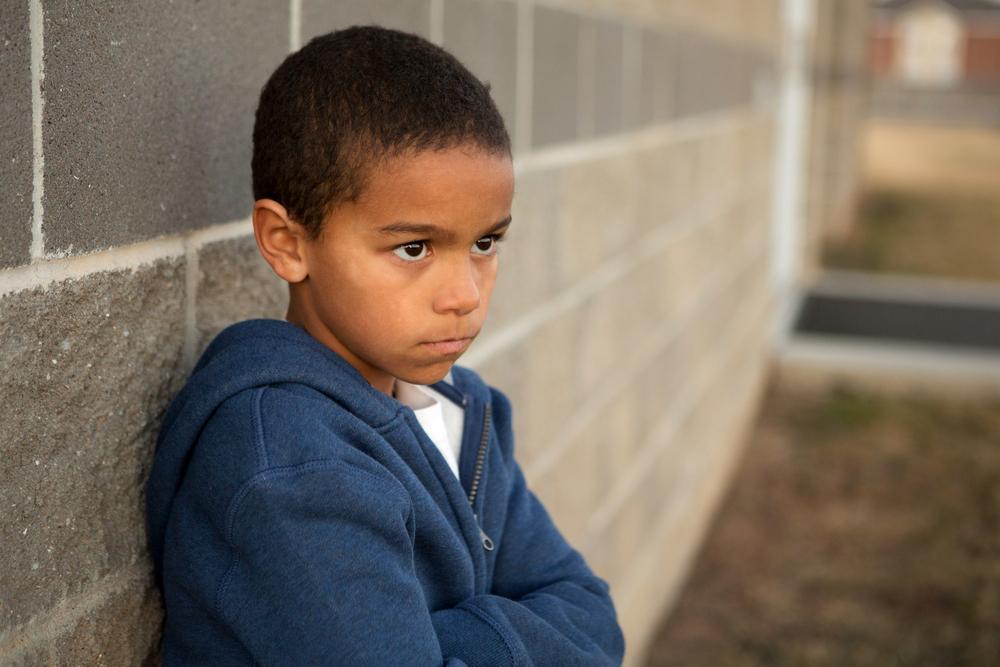 Young black boy leaning on wall looking upset.