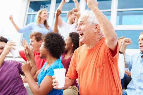 An older man cheering from the bleachers of a sport game.