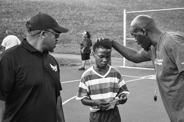 Male coach talking to young soccer athlete in black and white.