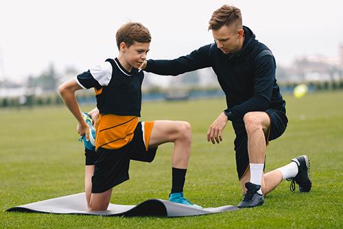 Male coach helping young male athlete stretch quads.