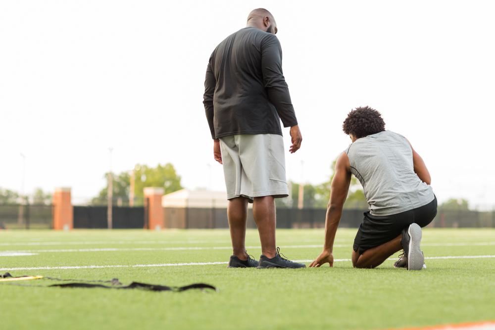 Black male coach talking to young teen male athlete.