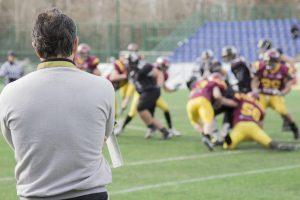 Older male coach watching football game.