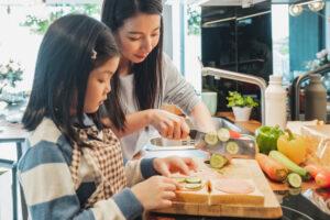 Mom helping prep sandwiches with young daughter.