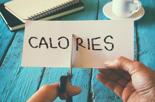 hand cutting a piece of paper with the word "calories" written on the paper.