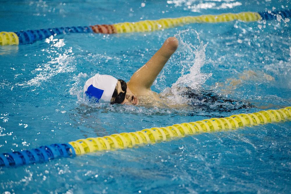 Young boy with missing arm swimming in a pool competitively.