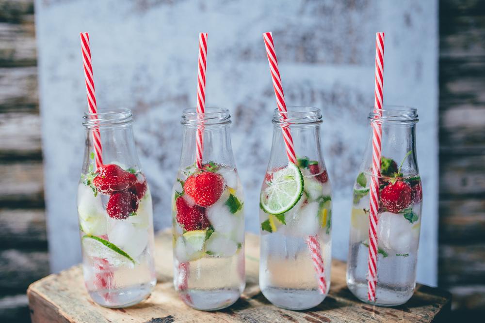 Glasses of water with straws, fruit and ice.