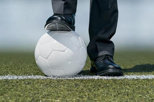 Close up of a man wearing dress shoes standing on a soccer ball.