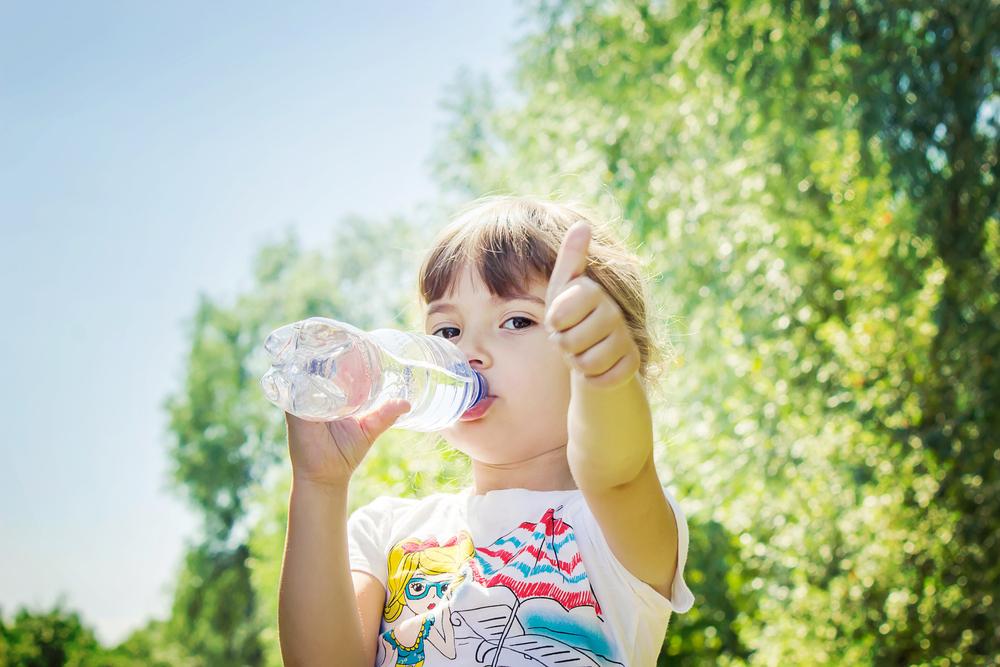 Young girl drinking water from a bottle and giving a thumbs up.