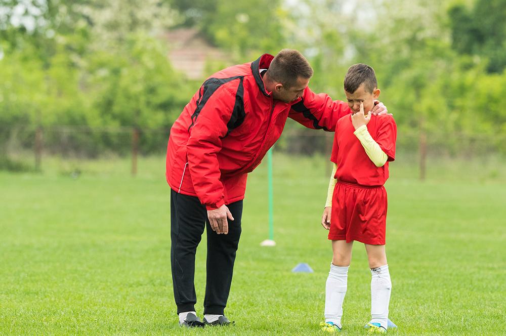 Male coach upsets young male player on soccer field.