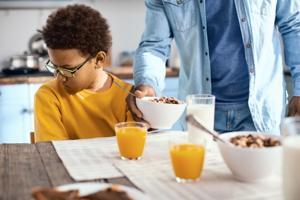 Young boy looking away from bowl of food being delivered by parent.