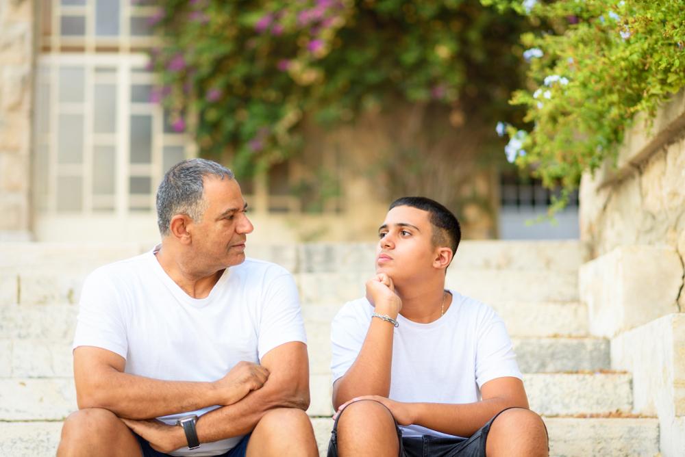 Father talking to teen son on outdoor steps.