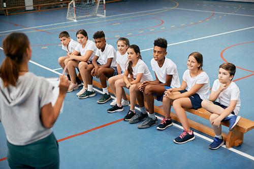 Female coach talking to team of boys and girls in gym.