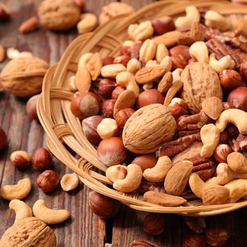 Woven bowl of various nuts on wooden table.