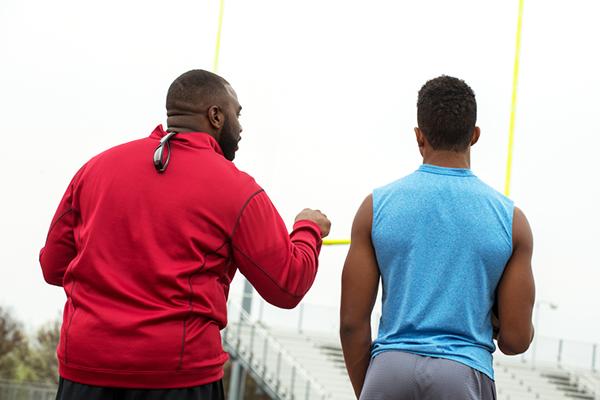 Football coach talking to teen male athlete alone.