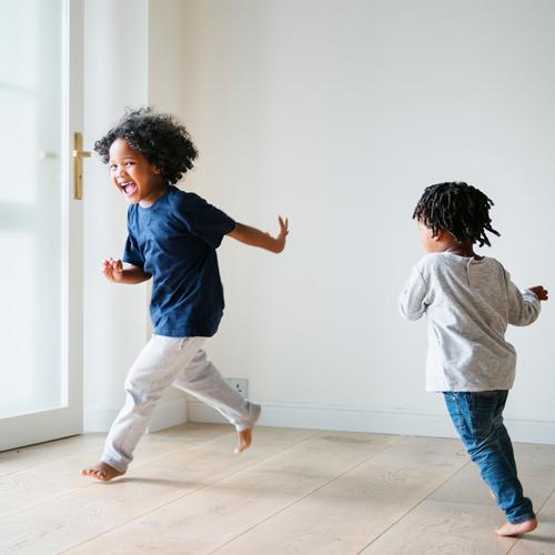 Two black children happily running around a house.