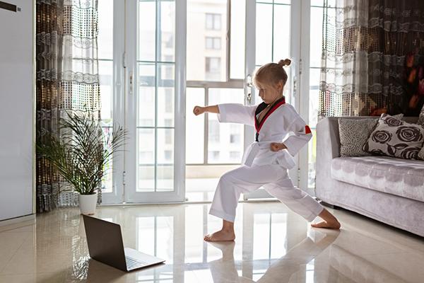 Young white girl doing taekwondo in her living room watching a laptop screen.