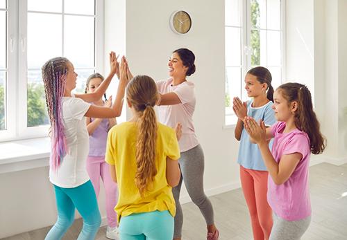 Pre-teen girls in workout gear high fiving with coach.