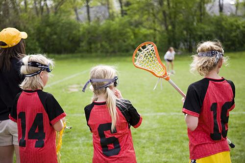 Young female lacrosse players on sideline with female coach.