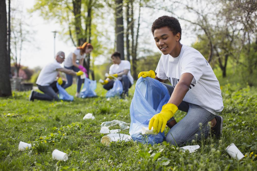 Young boy picking up trash with friends wearing gloves.