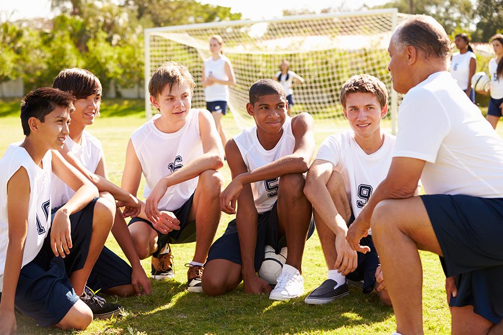 Male coach talking to diverse group of male teen soccer players.