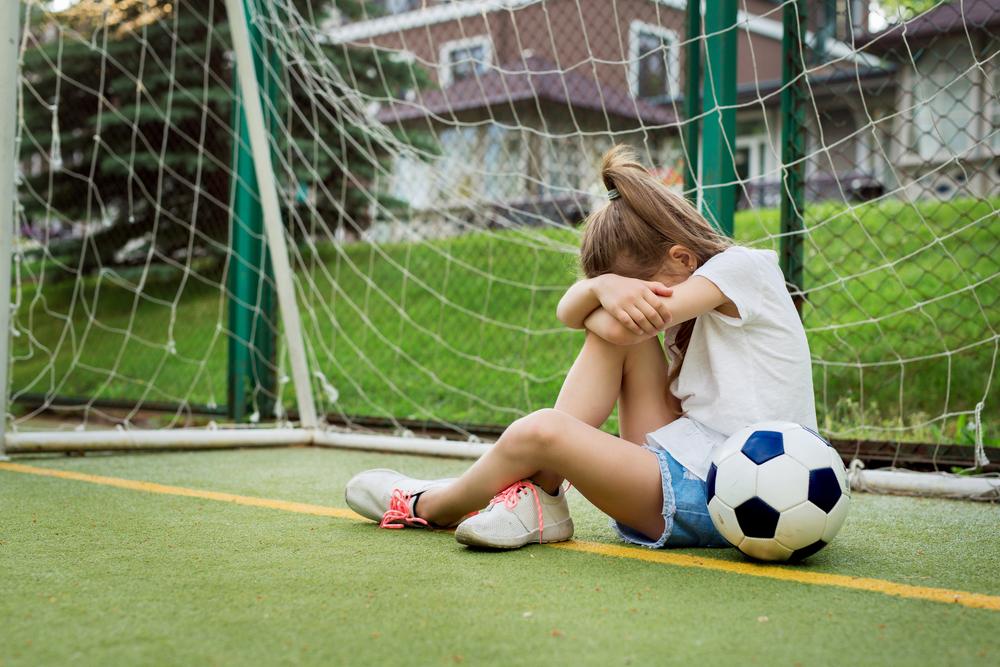 Upset young girl in front of goal next to soccer ball.