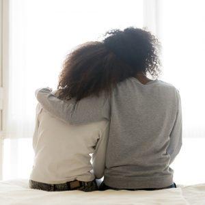 Rear view of black mother hugging daughter while sitting.