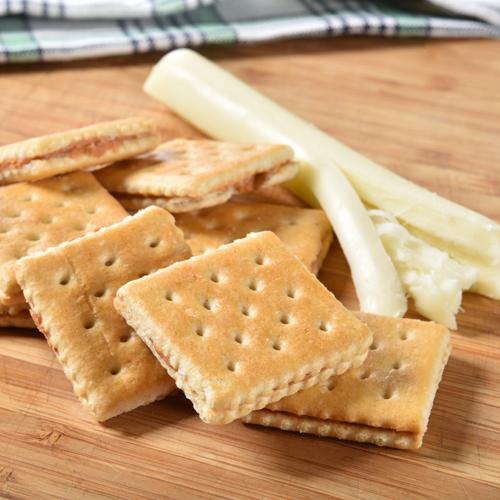 Close up view of cracker sandwiches and string cheese on a wood table top.