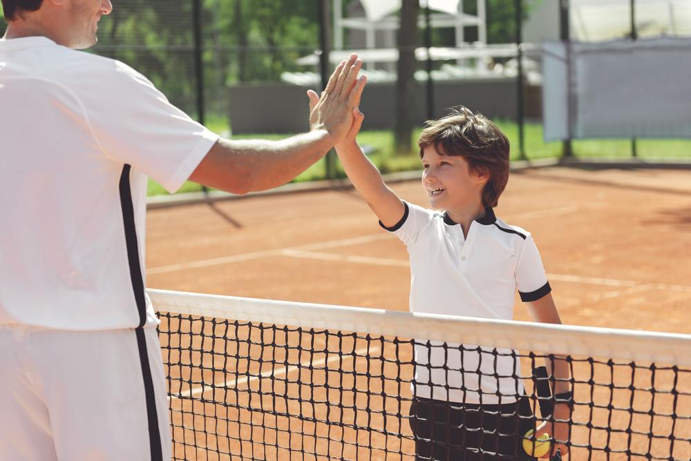 Young boy high fiving coach on tennis court.