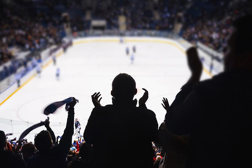 Fans shot in shadow from behind in a hockey arena.