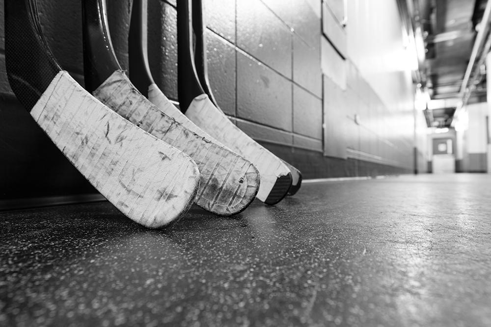 Hockey sticks lined up against a wall in a black and white image.