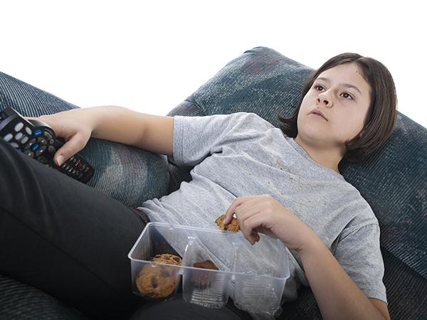 Young male child sitting in recliner eating cookies while holding a television remote.