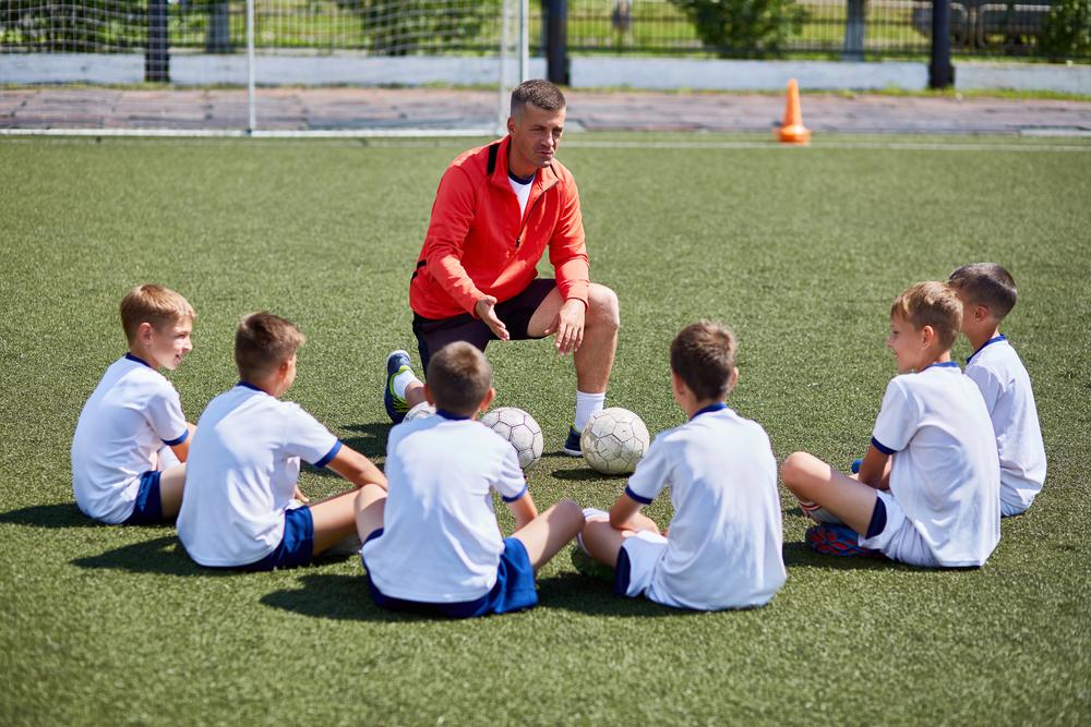 Coach talking to young male sports team on field.