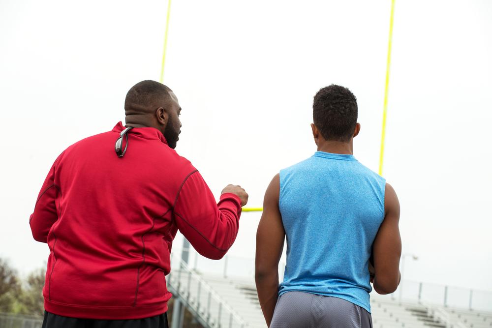 Coach talking solo to young football player after practice.