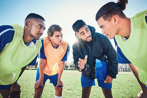 Male coach talking to older teen male athletes on field.