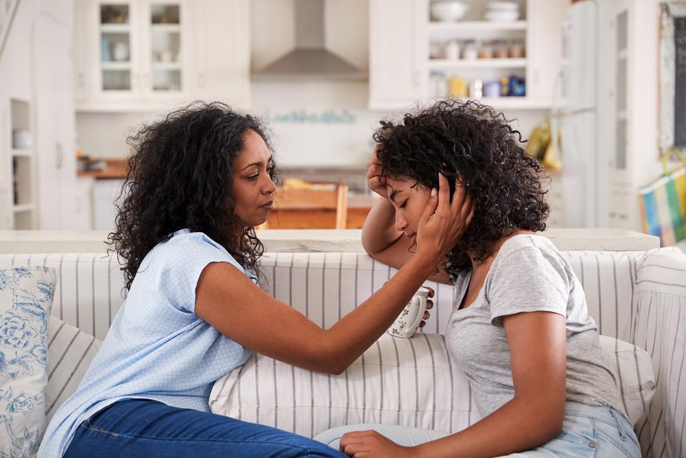 Mother comforting teen daughter on a couch.