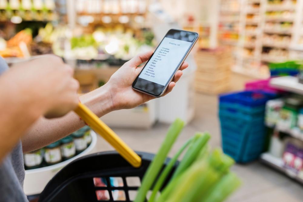 A hand holding a phone with a grocery list on it in a grocery store.