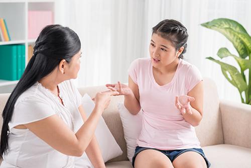 Mother and teen daughter arguing on a couch.