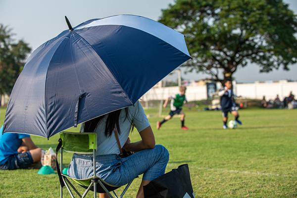 Mother sitting on sideline of outdoor soccer game.