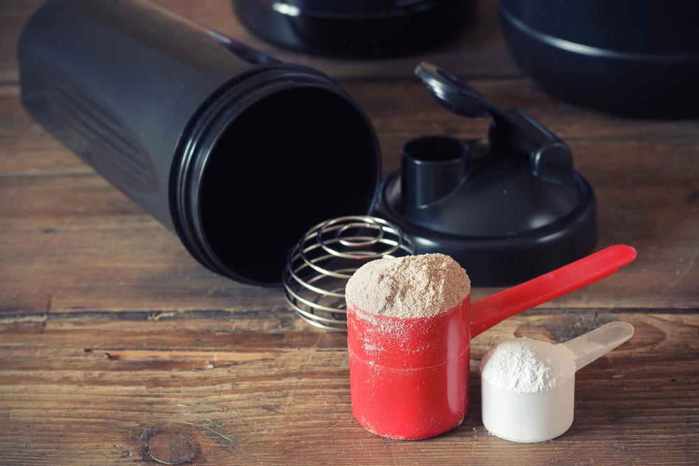 Powder supplements in cups next to an empty black water bottle.