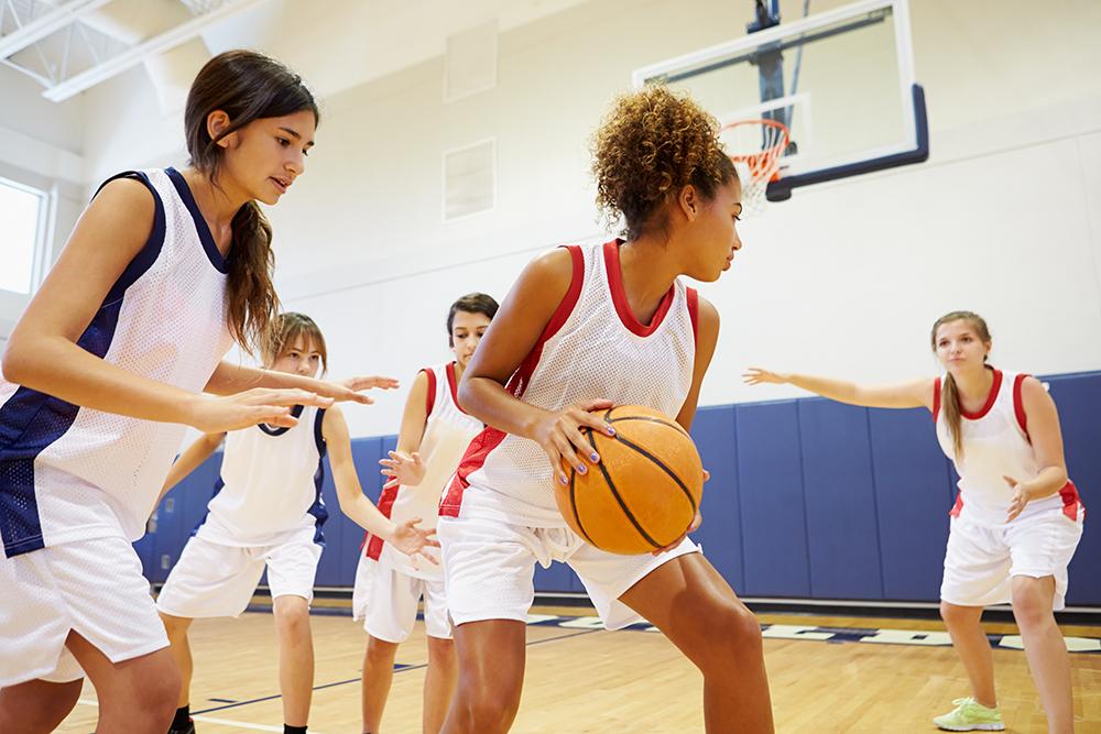 Diverse group of teen girls playing basketball indoors.